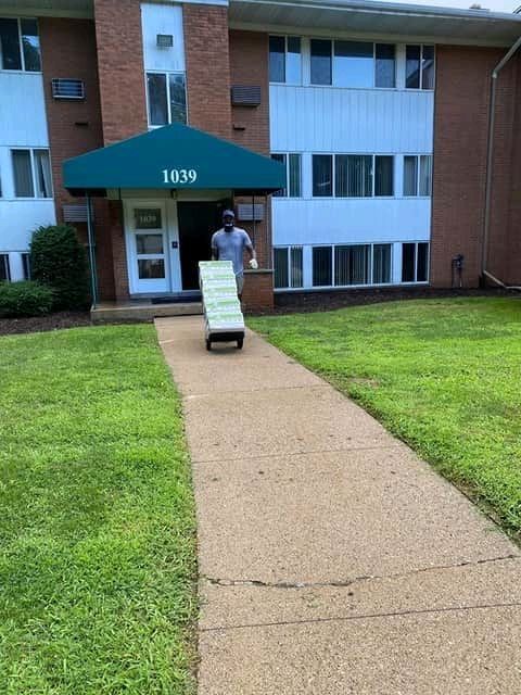 Sammy wheeling a stack of boxes on a hand truck out of an apartment building