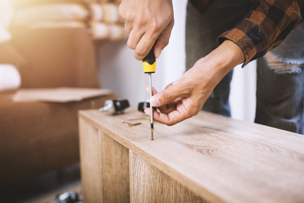 Hands assembling a wood furniture piece with a screwdriver
