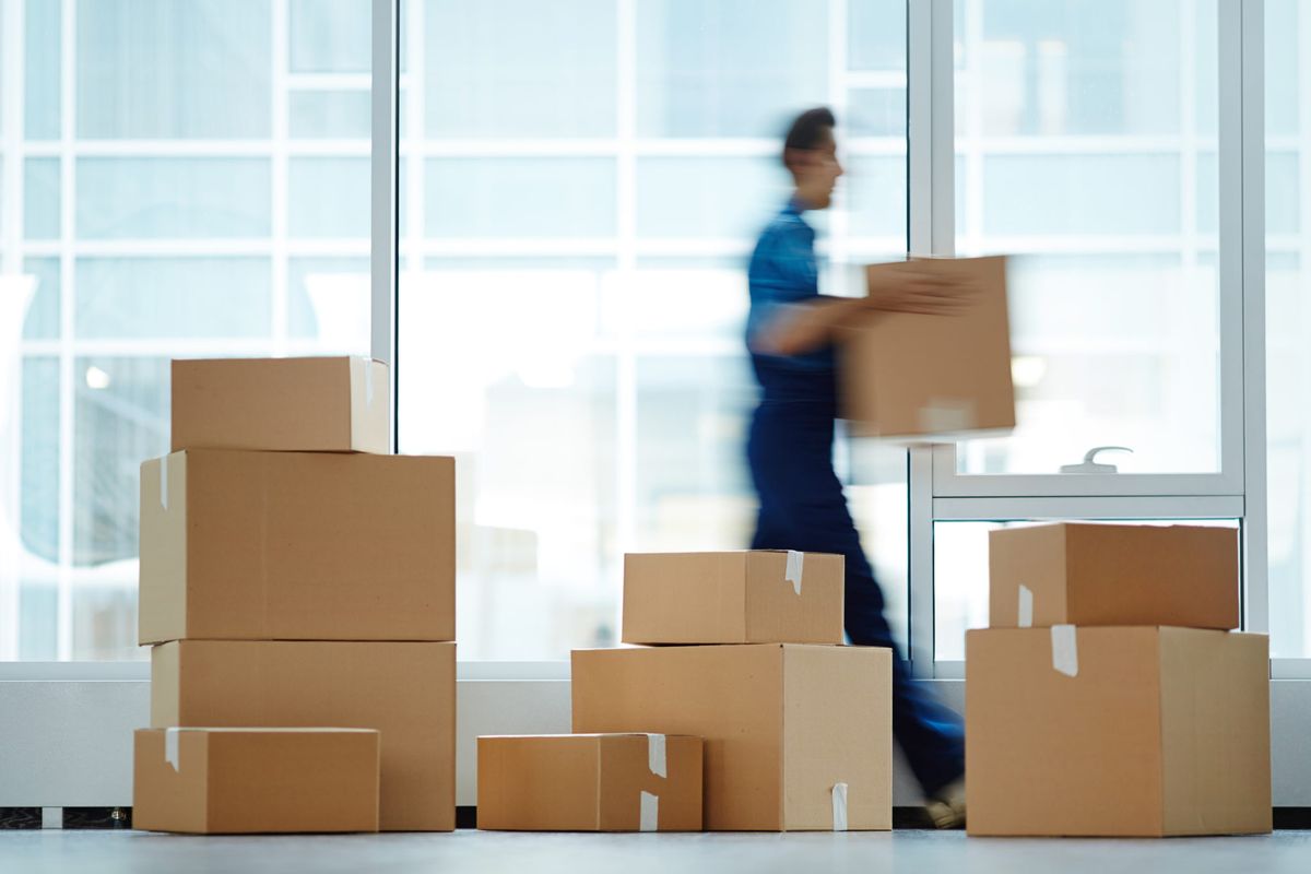 A mover carrying boxes past a stack of packed cartons